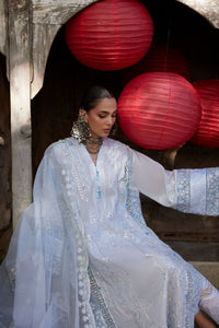 Woman in a light blue embroidered dress sitting in front of red lanterns.