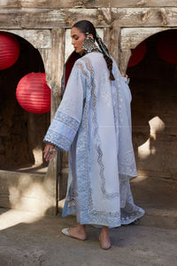 Woman in a light blue embroidered dress standing in front of a wooden structure with red lanterns.