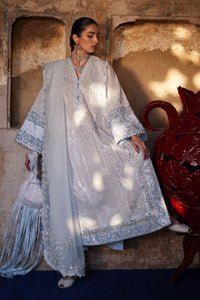 Woman in a light blue embroidered traditional outfit standing against a textured wall.