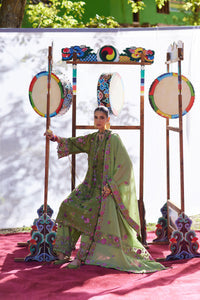 Traditional musician in a green outfit playing a drum with decorative stands in the background.