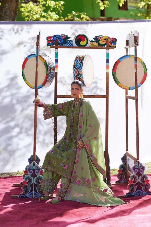Traditional musician in a green outfit playing a drum with decorative stands in the background.