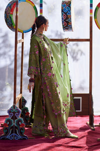 Woman in a green embroidered traditional outfit standing in front of decorative drums.