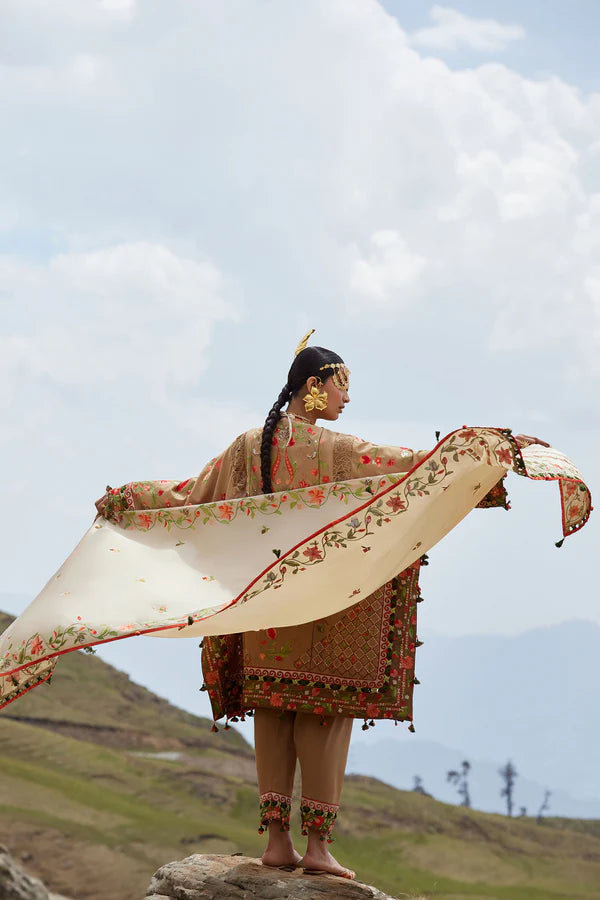 Woman in traditional attire holding a large embroidered scarf against a mountainous landscape.