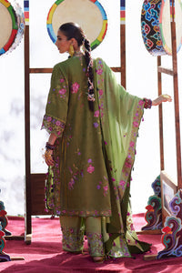 Woman in a green embroidered traditional outfit standing in front of decorative drums.