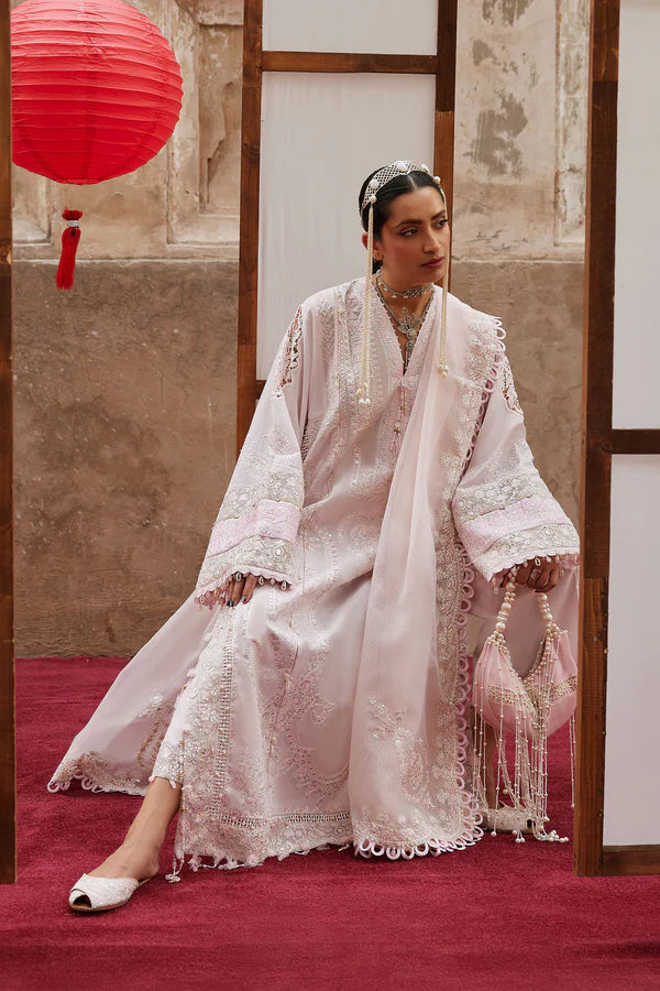 Woman in a traditional embroidered outfit sitting on a red carpet with a red lantern in the background.