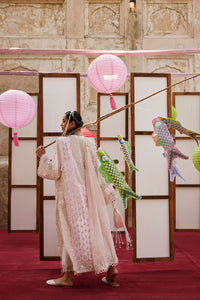 Woman in a light pink traditional outfit holding a rod with pink paper lanterns and colorful birds in front of a decorative screen.
