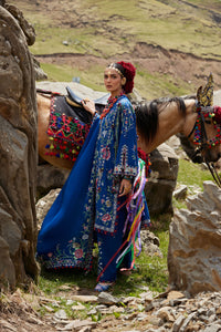Woman in traditional attire standing next to a horse in a mountainous landscape