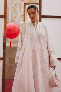 Woman in a long, light-colored dress standing indoors with a red lantern in the background.