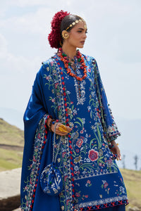 Woman in a blue embroidered traditional outfit with floral patterns against a mountainous background