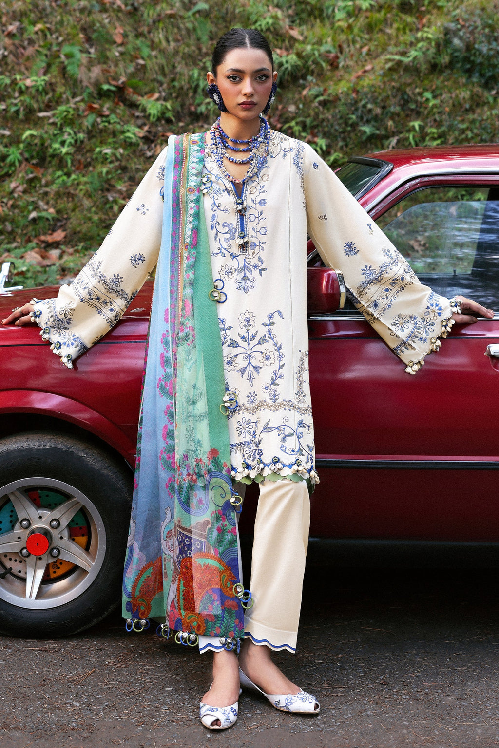 Woman in a traditional outfit standing next to a red car with a blurred natural background