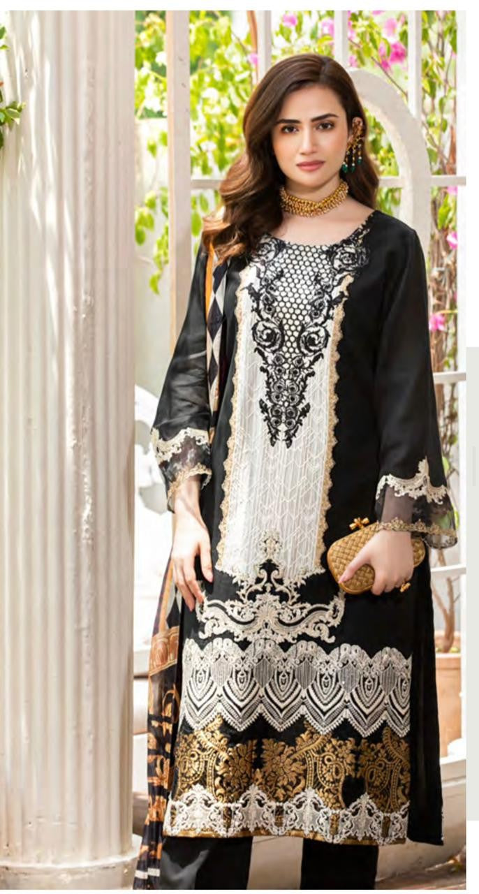 A woman modeling a black and white embroidered traditional kurta set with gold-patterned hem detailing, standing in front of a white arched doorway with green foliage visible in the background.