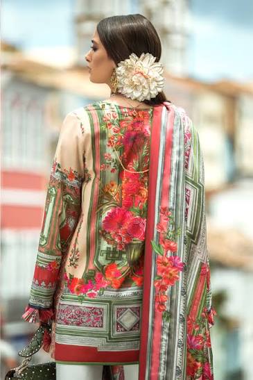 A woman shown from the back wearing a multicolor printed traditional outfit with a floral pattern, featuring a beige base with red, pink, and green designs, a matching dupatta, and a large white flower accessory in her hair.