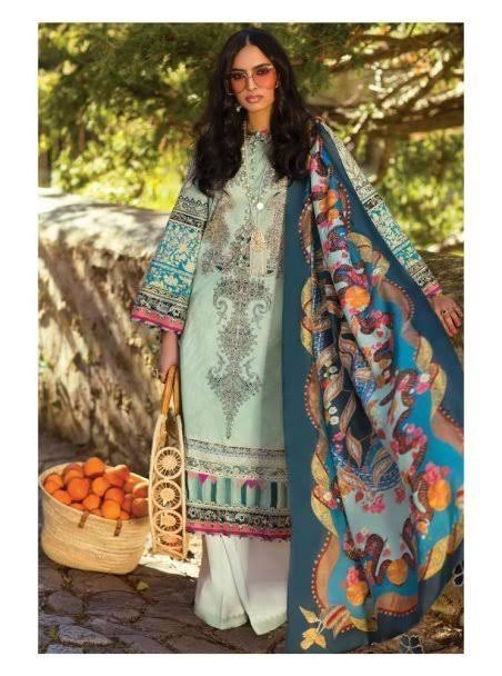 A woman stands outdoors wearing a light blue-green embroidered kurta with white pants and a large teal dupatta featuring colorful floral and paisley patterns. She holds a woven basket of oranges beside her.