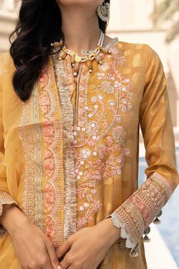 Woman wearing a mustard yellow embroidered outfit with pink details.