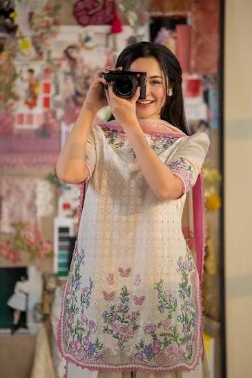 Woman taking a mirror selfie wearing a floral dress in a decorated room.