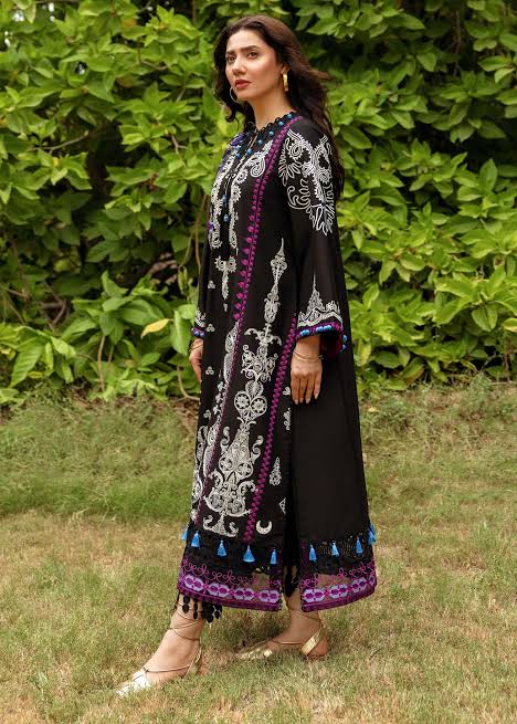 Woman wearing a black and white embroidered outfit with colorful patterns in a grassy area.