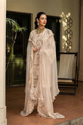 A woman models a traditional South Asian outfit featuring a cream-colored embroidered kurta with a matching sheer dupatta and a gold necklace, set against an elegant outdoor patio background.