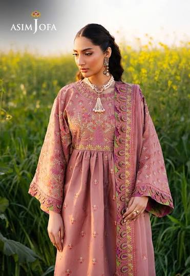 Woman in a pink embroidered outfit standing in a field with 'Asim Jofa' branding.