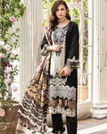 A woman models a traditional three-piece salwar kameez suit in black, white, and gold. The long-sleeve black kameez features intricate white and gold embroidery on the chest and hem, paired with a matching patterned dupatta and black trousers, set against a bright, sunlit garden patio background.