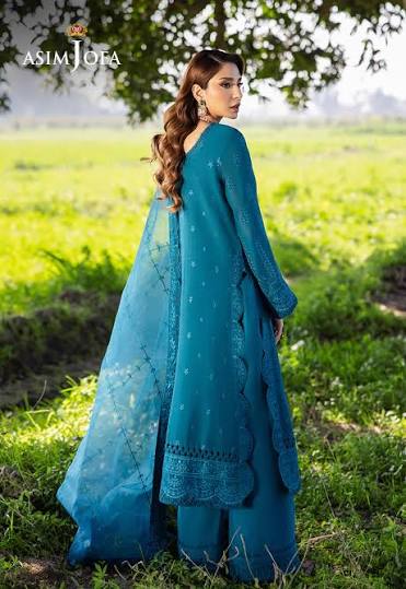 Woman in a teal outfit standing in a field with 'Asim Jofa' branding.