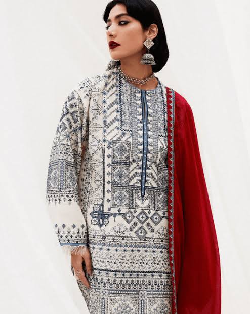 A woman modeling a traditional South Asian outfit featuring a cream-colored kurta with intricate black and blue geometric patterns, paired with a vibrant red dupatta.