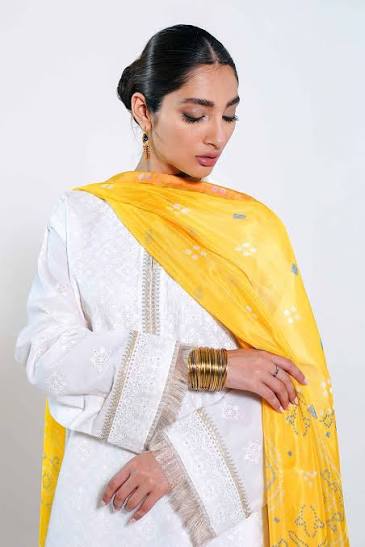 Woman wearing a white outfit with a yellow dupatta against a plain background