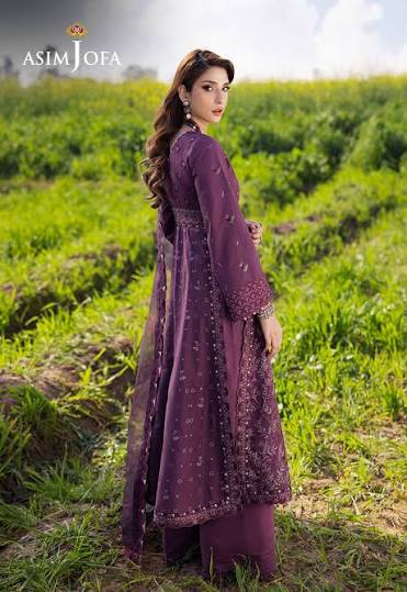 Woman in a purple traditional outfit standing in a field with 'Asim Jofa' branding.