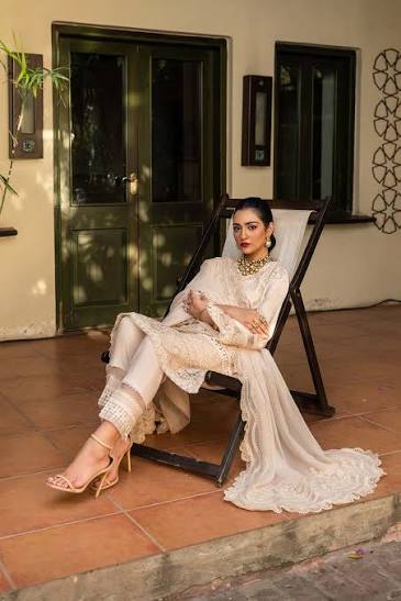 Woman in a white outfit sitting on a chair outdoors.