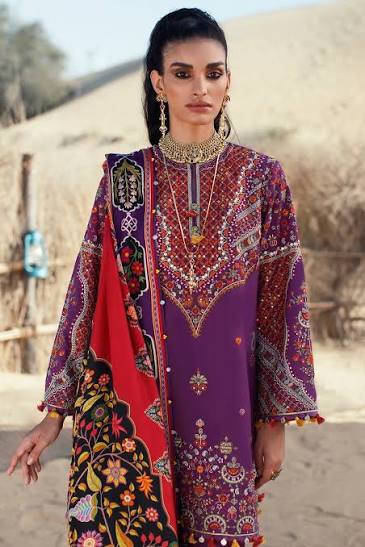 A woman modeling a purple embroidered ethnic kurta with a red and black floral dupatta, set against a sandy outdoor background.