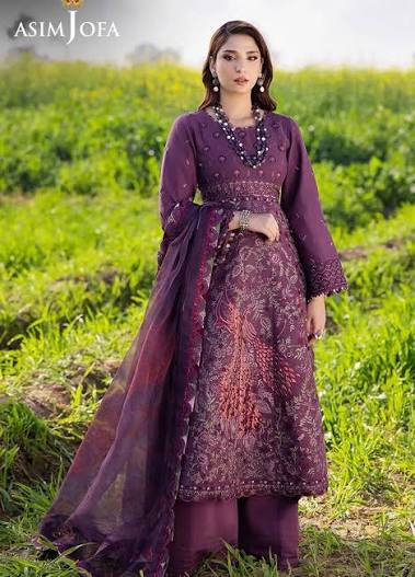 A woman stands outdoors in a grassy field wearing a deep purple embroidered traditional outfit with a matching sheer dupatta. The outfit features intricate floral embroidery and beadwork, and the brand name 'ASIM JOFA' is visible in the top left corner.