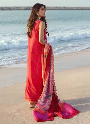 Woman in a red saree standing on a beach with ocean waves in the background