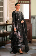 A woman models a black three-piece traditional outfit with pink and white floral embroidery, featuring a long kurta, matching trousers, and a sheer dupatta, set against an ornate indoor background.
