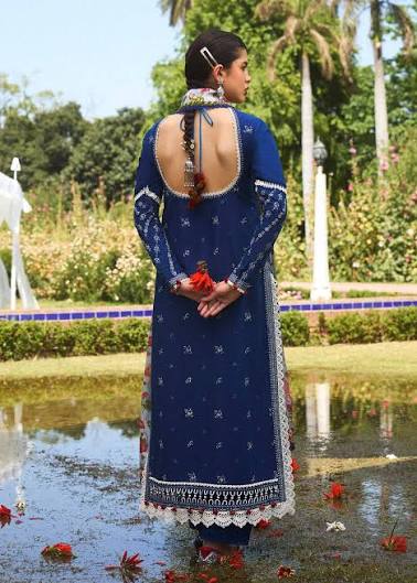 Woman in a blue traditional outfit standing by a pond with greenery in the background