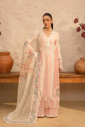 A woman models a traditional light pink ethnic outfit with intricate white embroidery and a matching sheer white dupatta featuring floral prints, set against a rustic beige wall with terracotta pots.