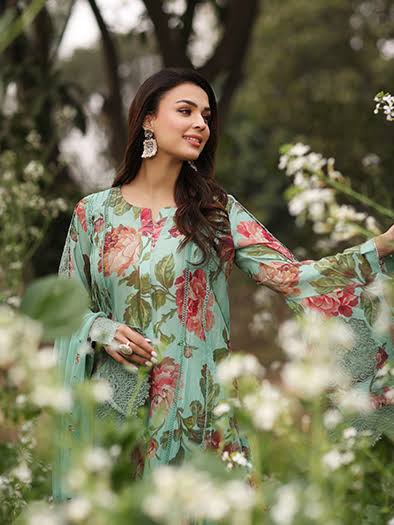 A woman wearing a mint green floral printed kurta with pink and red flowers, standing in a garden with white flowers in the foreground.