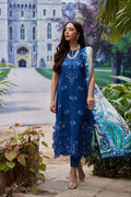Woman in a blue embroidered dress standing in front of a castle-like building.