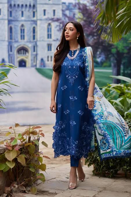 Woman in a blue embroidered dress standing in front of a castle-like building.