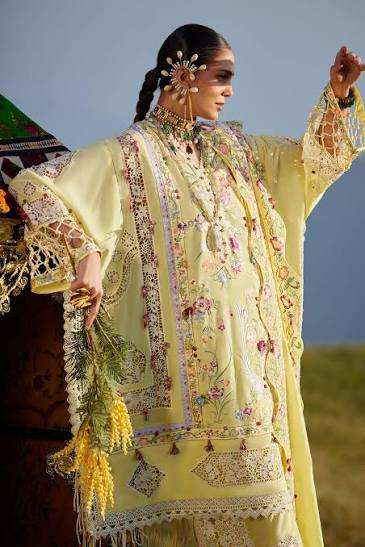 Woman in traditional embroidered yellow outfit with floral patterns against a clear sky.