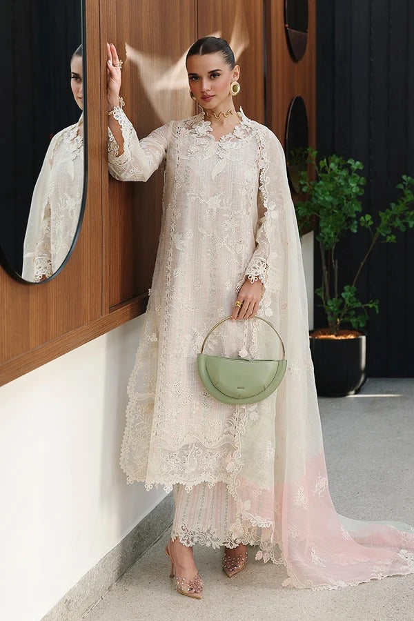 A woman models a traditional cream-colored embroidered kurta set with a matching sheer dupatta and light pink gradient underlayer, holding a sage green handbag.