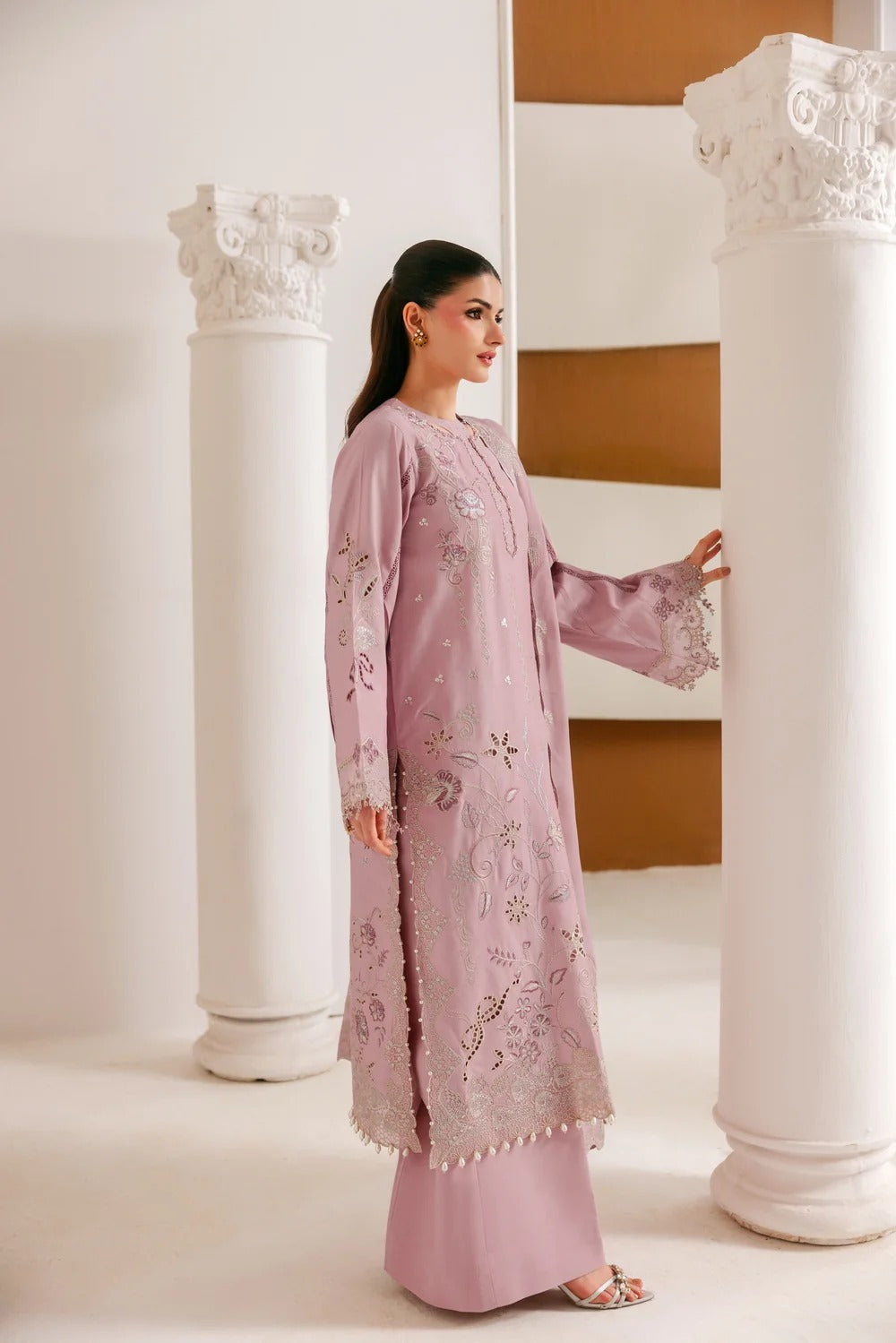 A woman modeling a lavender pink embroidered kurta and matching trousers in a classical architectural setting with white columns.