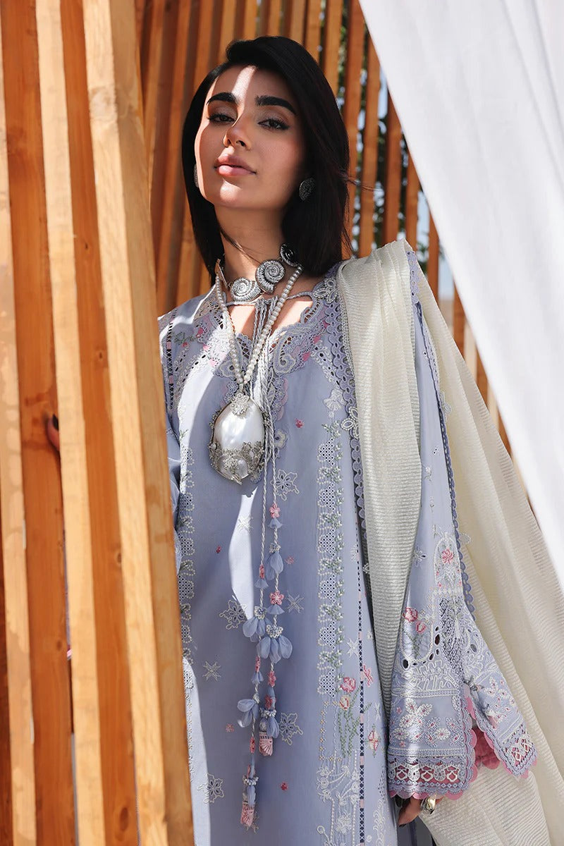 Woman wearing a light blue embroidered outfit with a white dupatta, standing against a wooden and white fabric background.