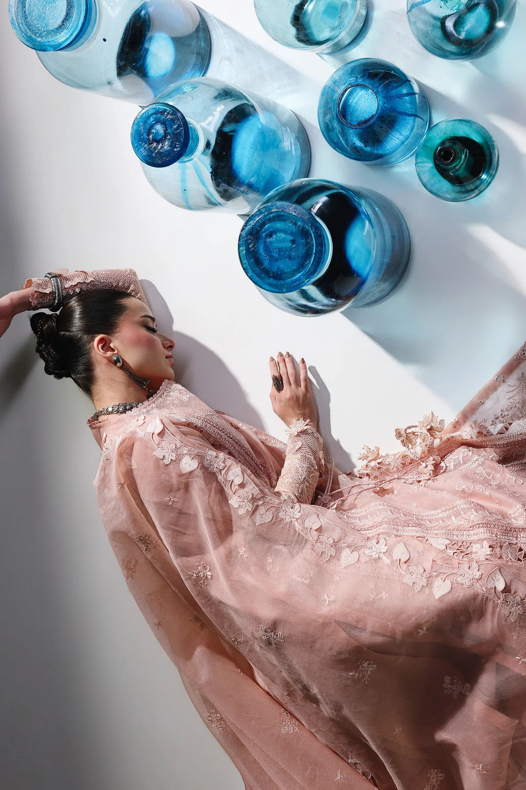 Woman in a pink dress lying on a white surface with blue bottles above her.