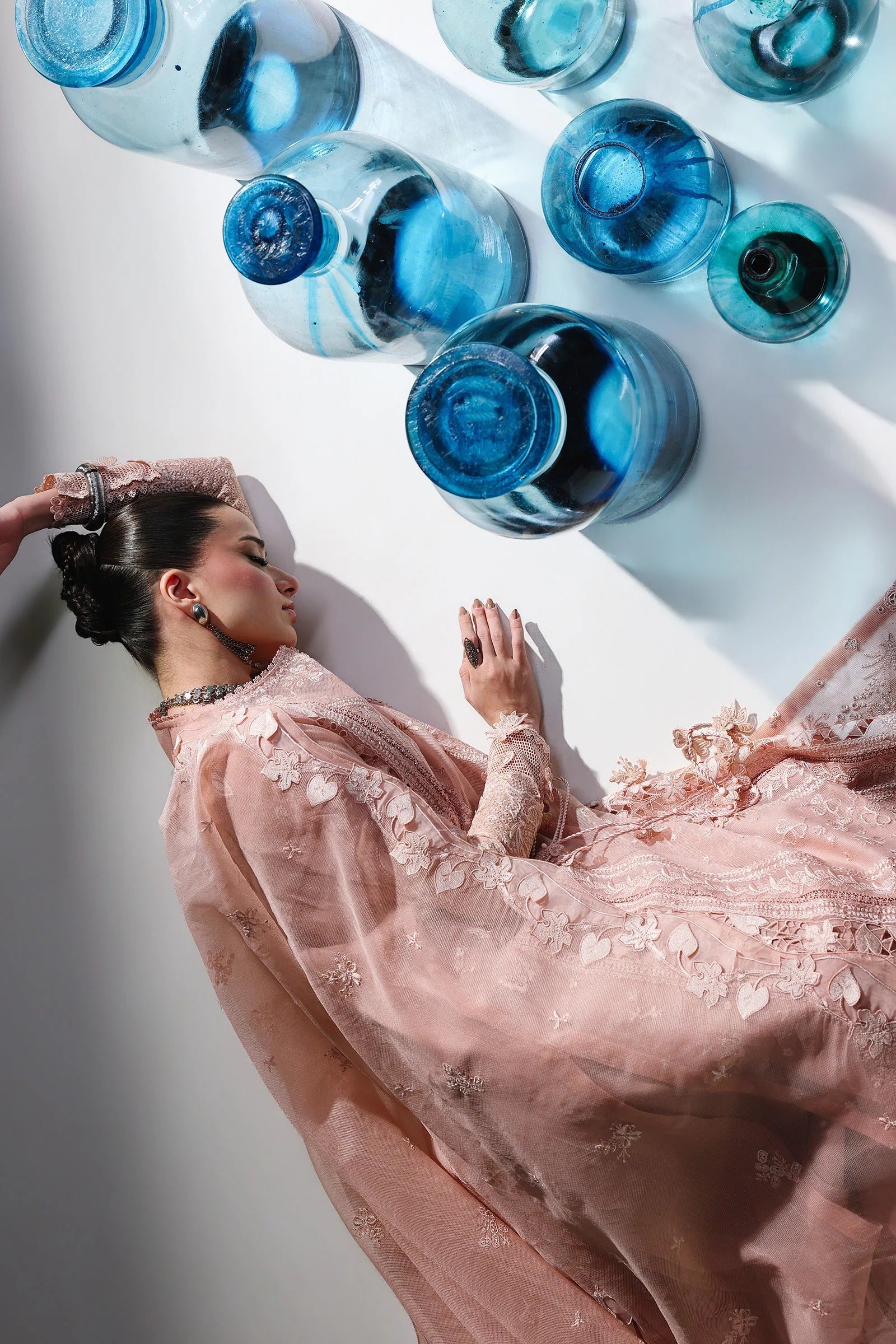 Woman in a pink dress lying on a white surface with blue bottles above her.