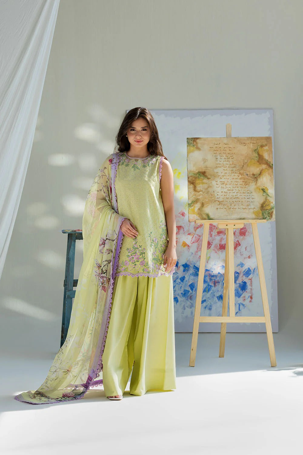 Woman in a light green traditional outfit standing next to a floral painting on an easel.