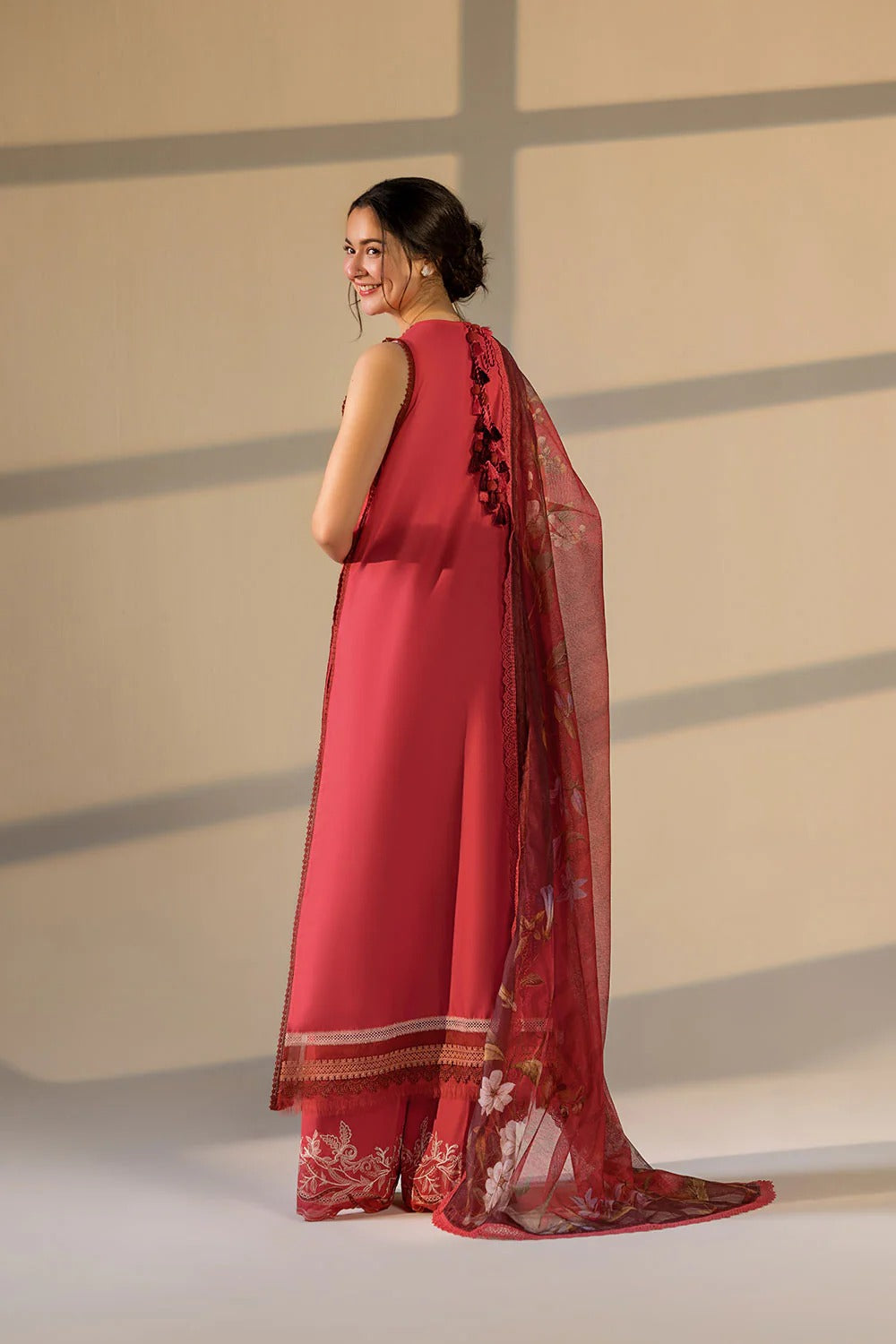 Woman wearing a red saree with a floral blouse against a neutral background