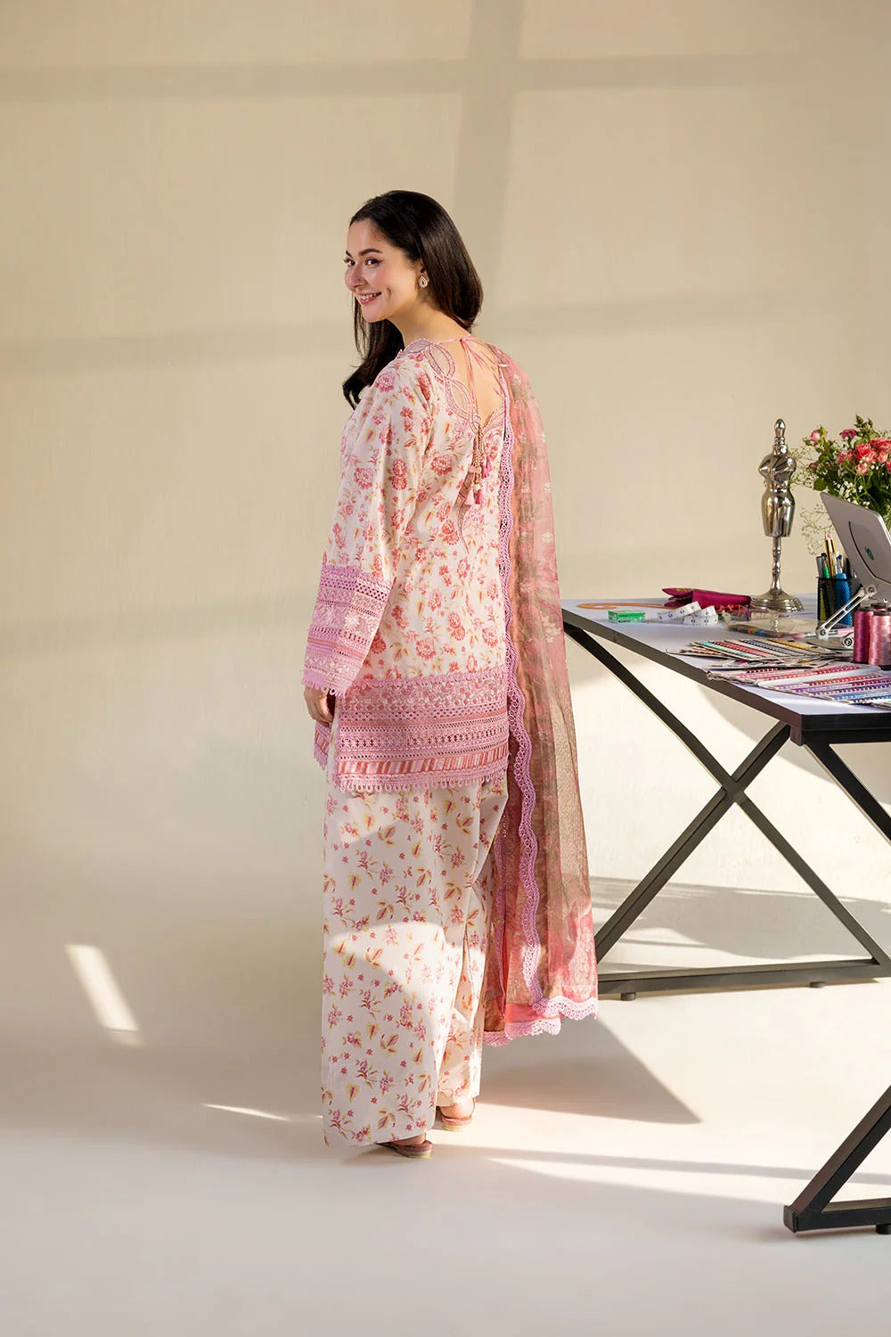 Woman in a floral outfit standing next to a table with decor items on a white background
