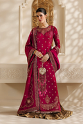 A woman models a traditional deep magenta pink Anarkali gown with intricate gold embroidery, a matching dupatta, and a gold pleated skirt, set against a warm beige background with decorative arches and soft shadow overlays.