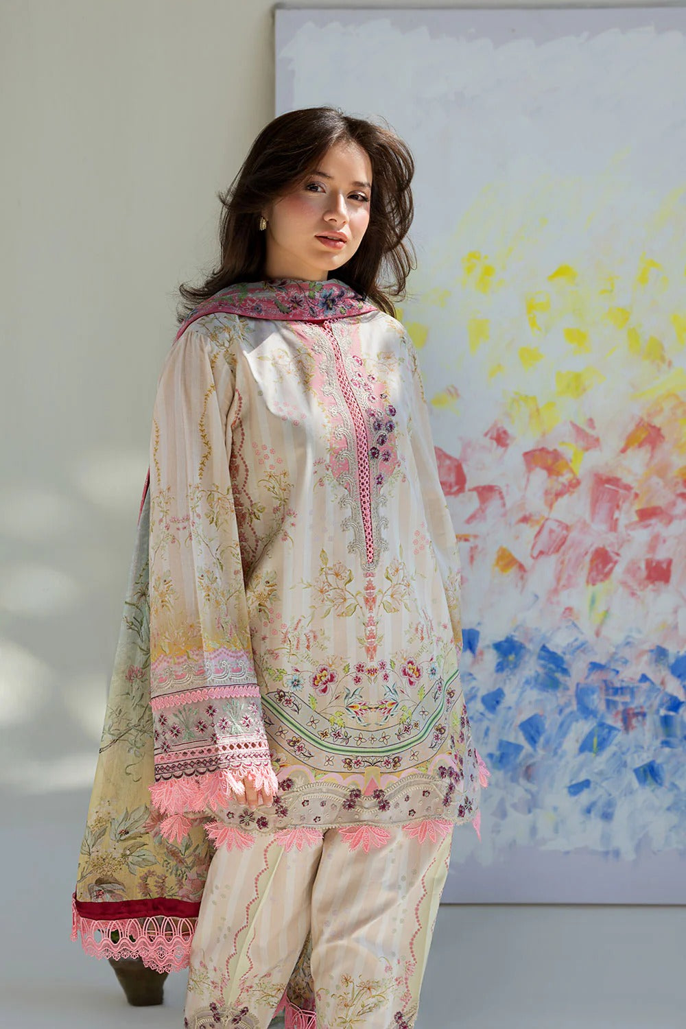 Woman wearing a floral embroidered outfit standing in front of a colorful abstract painting.