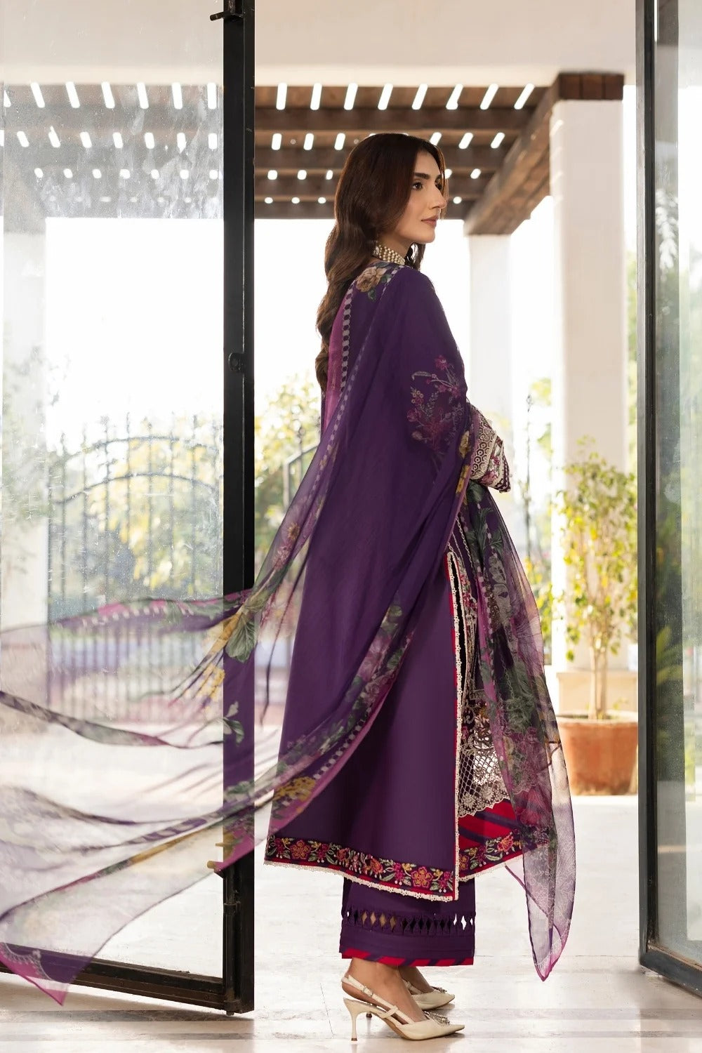 Woman in a purple traditional outfit with floral patterns standing in a modern interior setting.