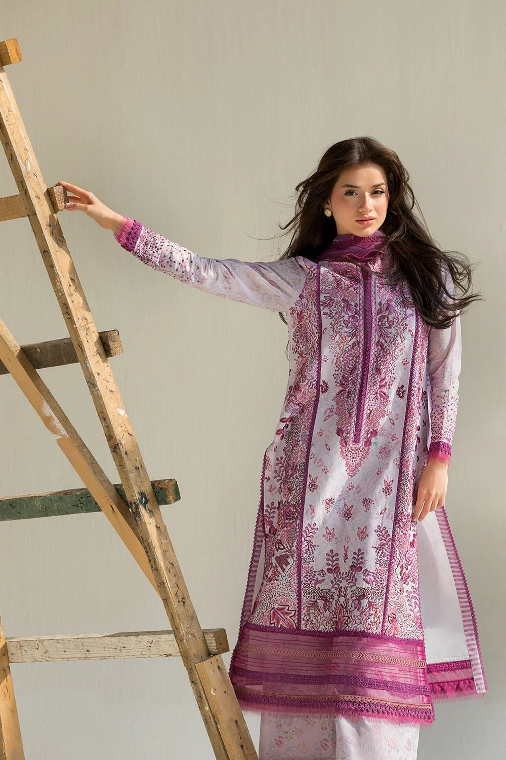 Woman in a white and purple traditional outfit standing next to a wooden ladder.